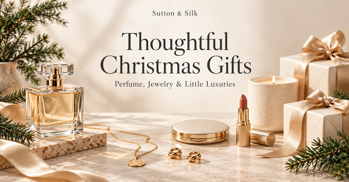 Sutton & Silk Christmas gift guide with perfume, gold jewelry, makeup, a candle, and ivory gift boxes surrounded by evergreen branches.